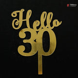 Gold metallic 'Hello 30' cake topper with a single stem, shown on a solid black background. A small 'Bakeyy' watermark is visible in the top right corner.