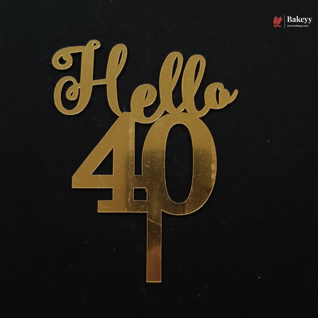 Gold metallic cake topper with the words 'Hello 40' in a cursive and block font, displayed on a solid black background.