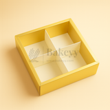 Gold bakery box with a clear lid on a beige background, featuring the brand 'Bakeyy'.