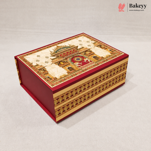 A decorative red and gold gift box with an intricate architectural illustration on the lid, photographed on a light gray background. The Bakeyy logo is visible in the top right corner.