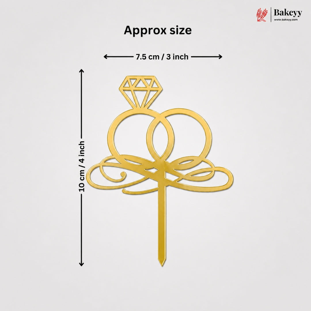 Gold ring cake topper with a diamond design and decorative scrollwork, shown with dimension lines indicating approximate size of 10 cm by 7.5 cm on a light gray background.