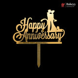 Gold acrylic 'Happy Anniversary' cake topper with a silhouette of a bride and groom on a black background, featuring a Bakeyy brand watermark in the top right corner.