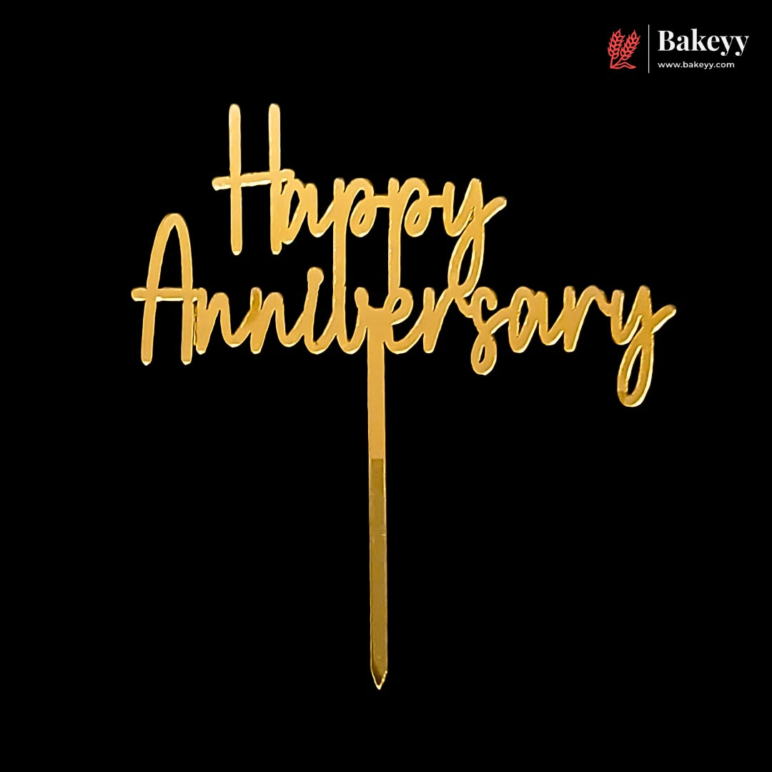 Gold acrylic 'Happy Anniversary' cake topper with a metal wire stake, shown against a solid black background. A Bakeyy logo is visible in the top right corner.