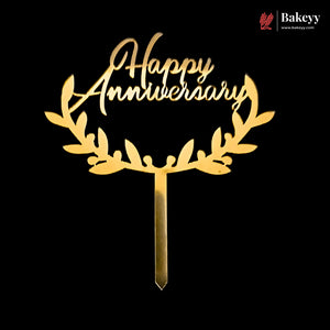 Gold laser-cut acrylic cake topper with 'Happy Anniversary' script and leafy wreath design on a black background, with a Bakeyy logo in the top right corner.