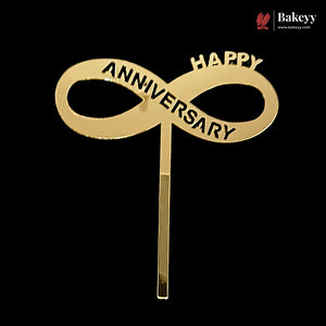 A gold-colored infinity loop cake topper with the words 'HAPPY ANNIVERSARY' engraved on it, set against a solid black background. A Bakeey brand logo is visible in the top right corner.