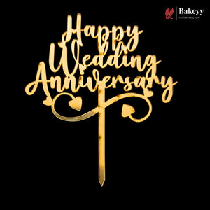 Gold wooden 'Happy Wedding Anniversary' cake topper with heart details and a stake, shown on a solid black background. A Bakeyy logo is visible in the top right corner.