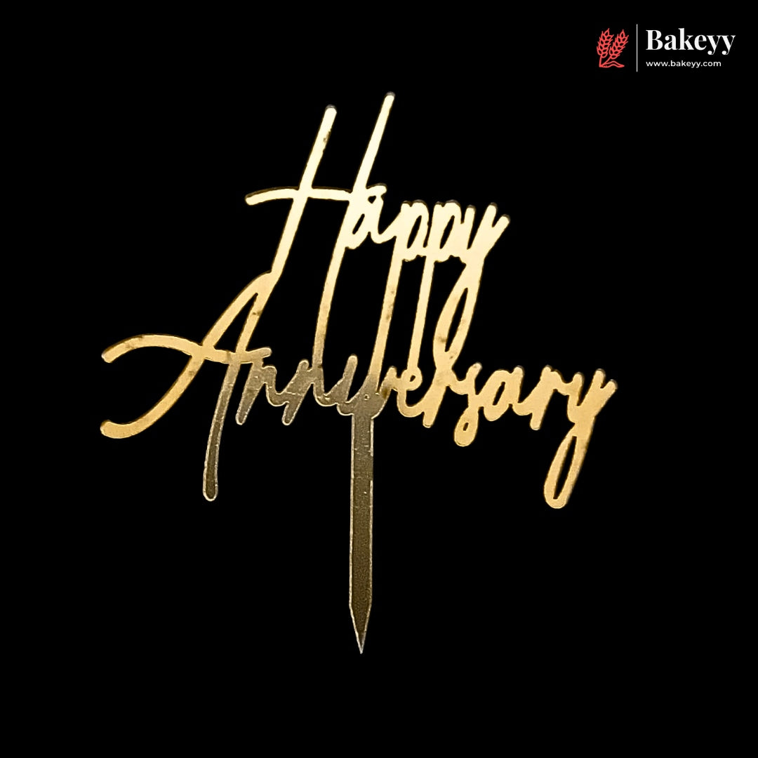 Gold metallic 'Happy Anniversary' script cake topper on a black background, with a Bakeyy logo in the top right corner.