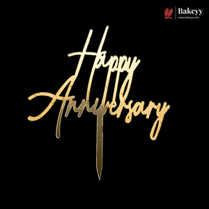 Gold metallic 'Happy Anniversary' script cake topper on a black background, with a Bakeyy logo in the top right corner.