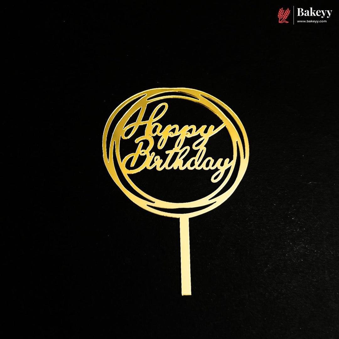 A gold metal 'Happy Birthday' cake topper with a circular cutout design and a straight stem, shown on a black background. A Bakeey brand logo is visible in the top right corner.