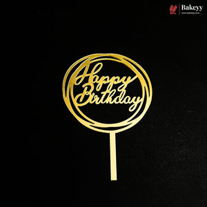 A gold metal 'Happy Birthday' cake topper with a circular cutout design and a straight stem, shown on a black background. A Bakeey brand logo is visible in the top right corner.