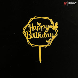 A gold metal 'Happy Birthday' cake topper with a geometric octagonal frame, decorative butterflies, and a stick, shown on a black background. A 'Bakeey' brand logo is visible in the top right corner.