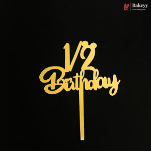 Gold metal cake topper with '1/2 Birthday' script on a black background, featuring a Bakeyy brand logo in the top right corner.