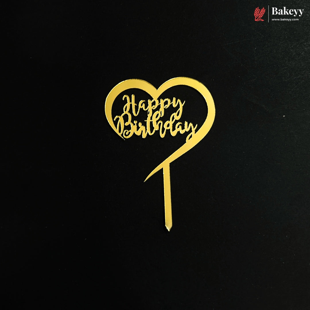 A gold heart-shaped cake topper with 'Happy Birthday' written in cursive script, displayed on a black background with a Bakeyy logo in the top right corner.