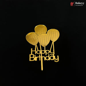 A gold-colored metal cake topper featuring three balloon shapes above the words 'Happy Birthday' in cursive, displayed on a solid black background. A 'Bakeyy' brand logo is visible in the top right corner.