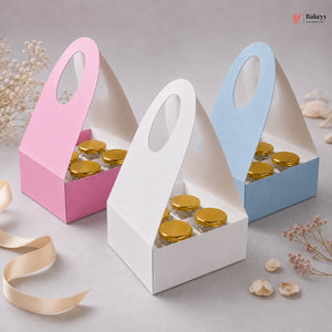 Three small cardboard boxes with gold lids, one pink, one white, and one blue, on a light gray background.