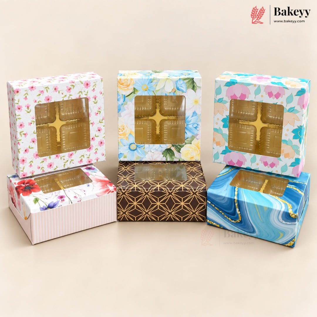 Five decorative bakery boxes with clear plastic window tops, arranged on a beige studio background. The boxes feature floral, striped, geometric gold patterns, and a blue marbled design.
