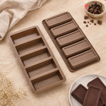 Two brown rectangular chocolate mold trays on a beige fabric surface, with a small bowl of chocolate chunks and chocolate bars used as styling props. No person or real environment is present, so this is Product/Packaging rather than Lifestyle.