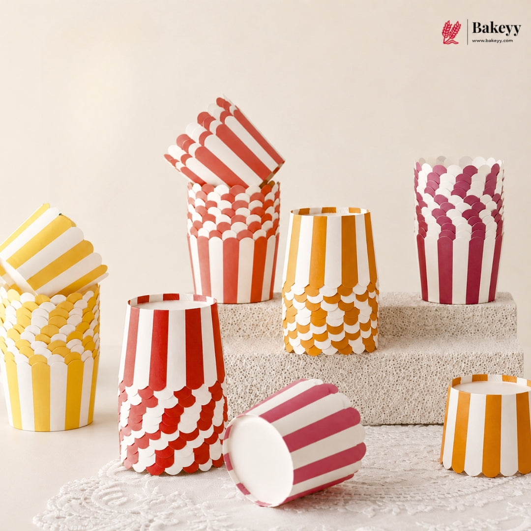 A set of paper popcorn bucket cups in red, yellow, orange, and pink, featuring striped and scalloped patterns, displayed on a textured stone block and lace runner.