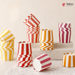A set of paper popcorn bucket cups in red, yellow, orange, and pink, featuring striped and scalloped patterns, displayed on a textured stone block and lace runner.