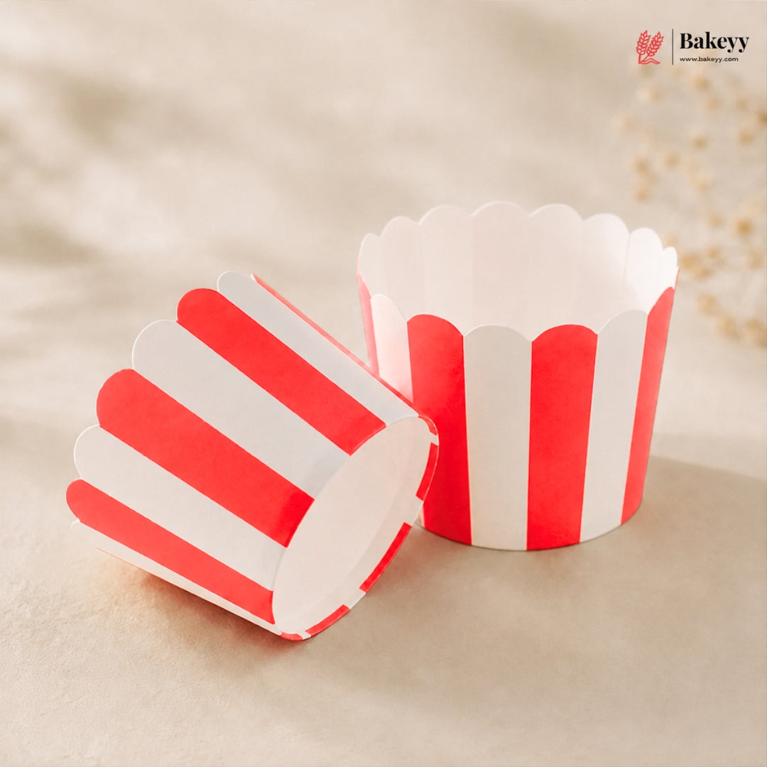 Two red and white striped scalloped paper cupcake liners, one standing upright and one lying on its side, on a beige textured background with a Bakeey logo in the top right corner.