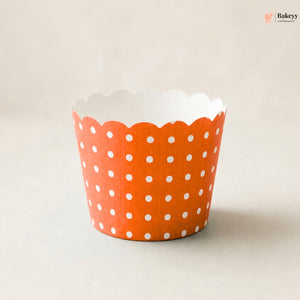 An orange paper cupcake liner with a white polka dot pattern and scalloped edge, photographed on a neutral light beige background.