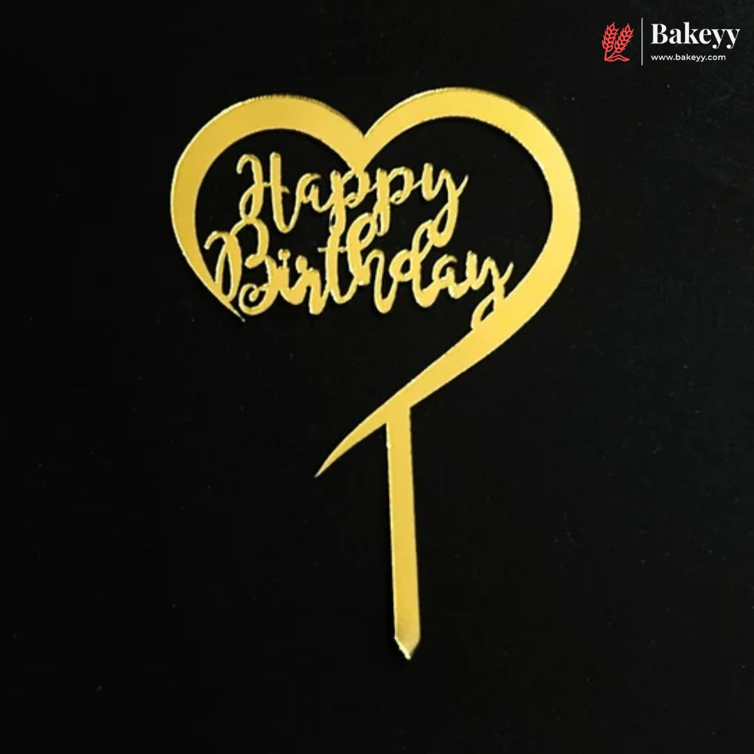 A gold heart-shaped cake topper with 'Happy Birthday' written in cursive script on a black background, with a Bakeey logo in the top right corner.