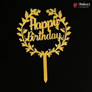 A gold metal 'Happy Birthday' cake topper with a leafy wreath design and a single stem, shown on a solid black background. A Bakeey brand logo is visible in the top right corner.