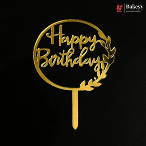 A gold-colored metal 'Happy Birthday' cake topper with a leafy wreath design on a black background, featuring a Bakeey brand logo in the top right corner.