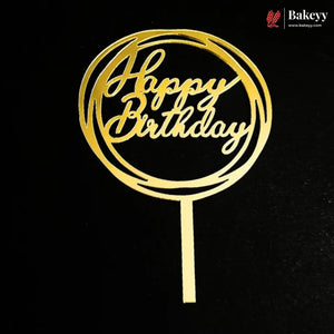A gold-colored metal 'Happy Birthday' cake topper with a circular design and a straight bottom stem, shown against a solid black background. A 'Bakeey' brand logo is visible in the top right corner.