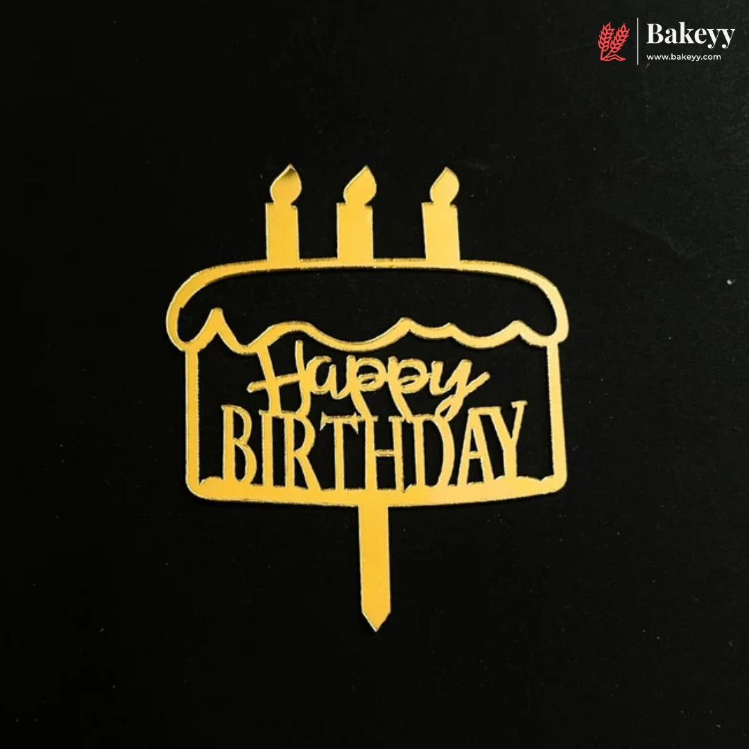 A gold metal cake topper shaped like a birthday cake with three candles and the words 'Happy Birthday' cut out in the center, displayed on a black background. The Bakeey brand logo is visible in the top right corner.