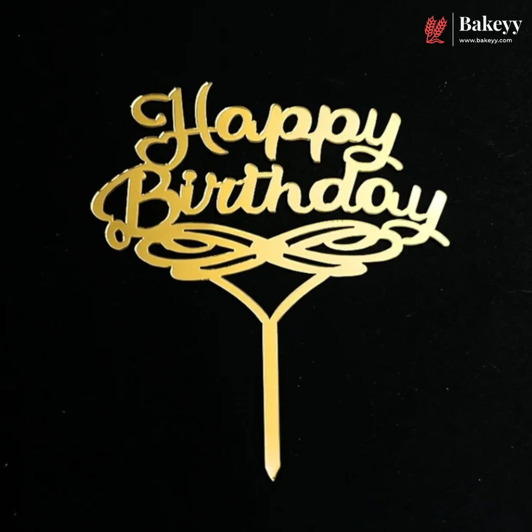 Gold metal 'Happy Birthday' cake topper with decorative swirls and a stick, shown on a black background. A Bakeey logo watermark is visible in the top right corner.