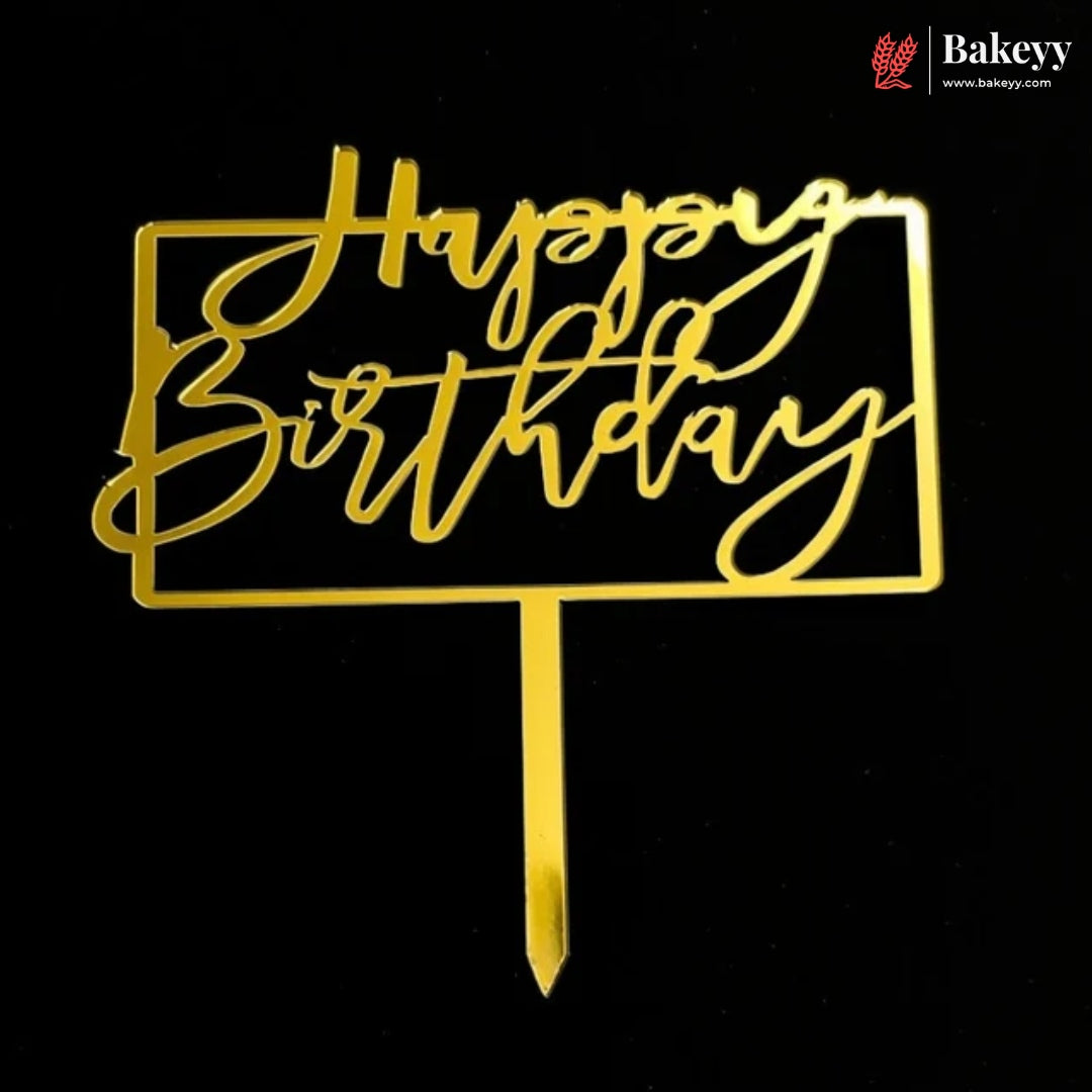 Gold metal 'Happy Birthday' cake topper with a rectangular frame and stick, shown on a black background. A Bakeey logo is visible in the top right corner.