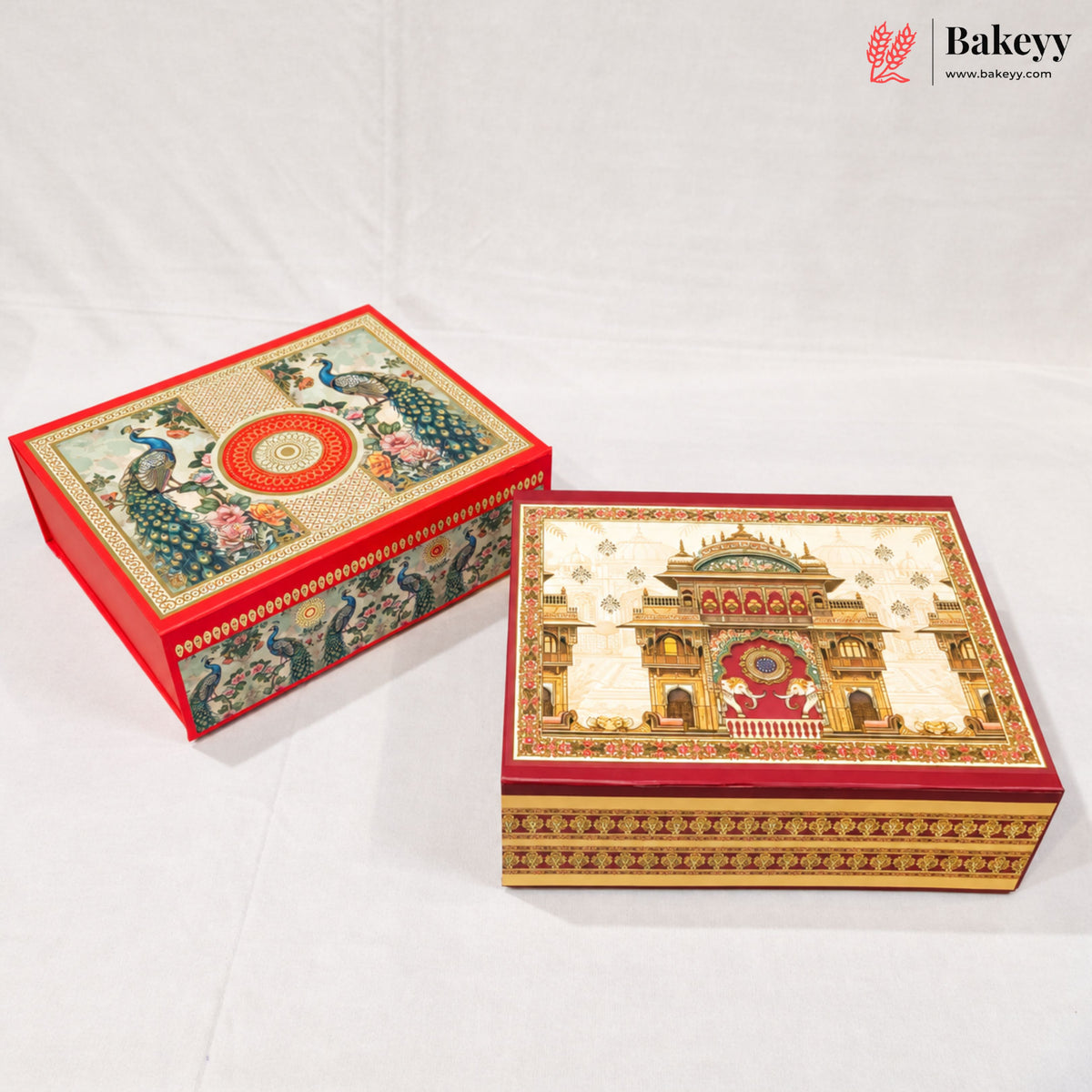 Two ornate decorative gift boxes with intricate hand-painted traditional Indian designs, one featuring peacocks and the other a palace motif, displayed on a white fabric background.