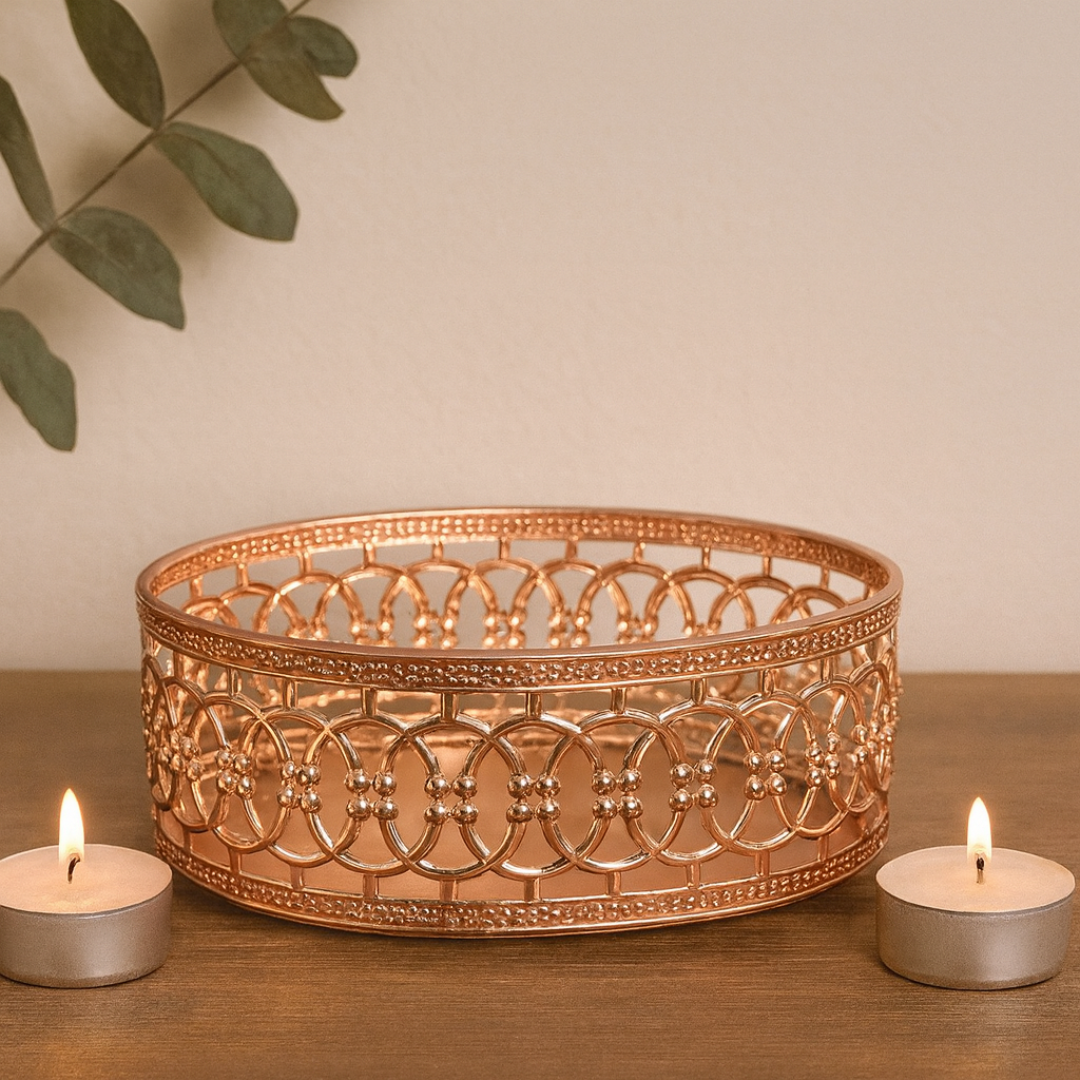 Decorative copper bowl with two lit tealights on a wooden surface.