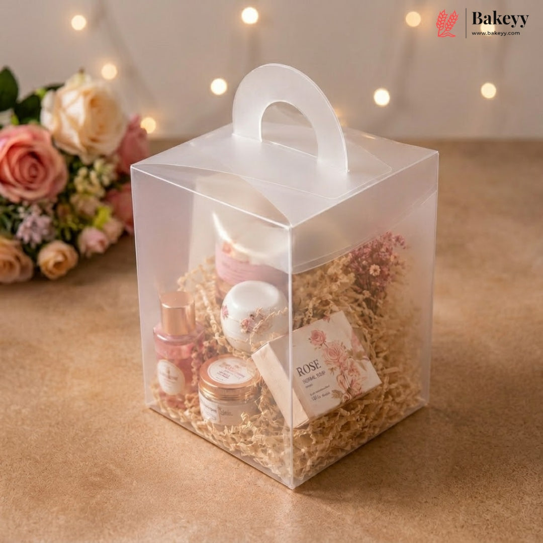 Clear gift box with cosmetic products and flowers on a wooden surface with blurred lights in the background
