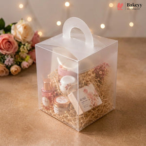Clear gift box with cosmetic products and flowers on a wooden surface with blurred lights in the background