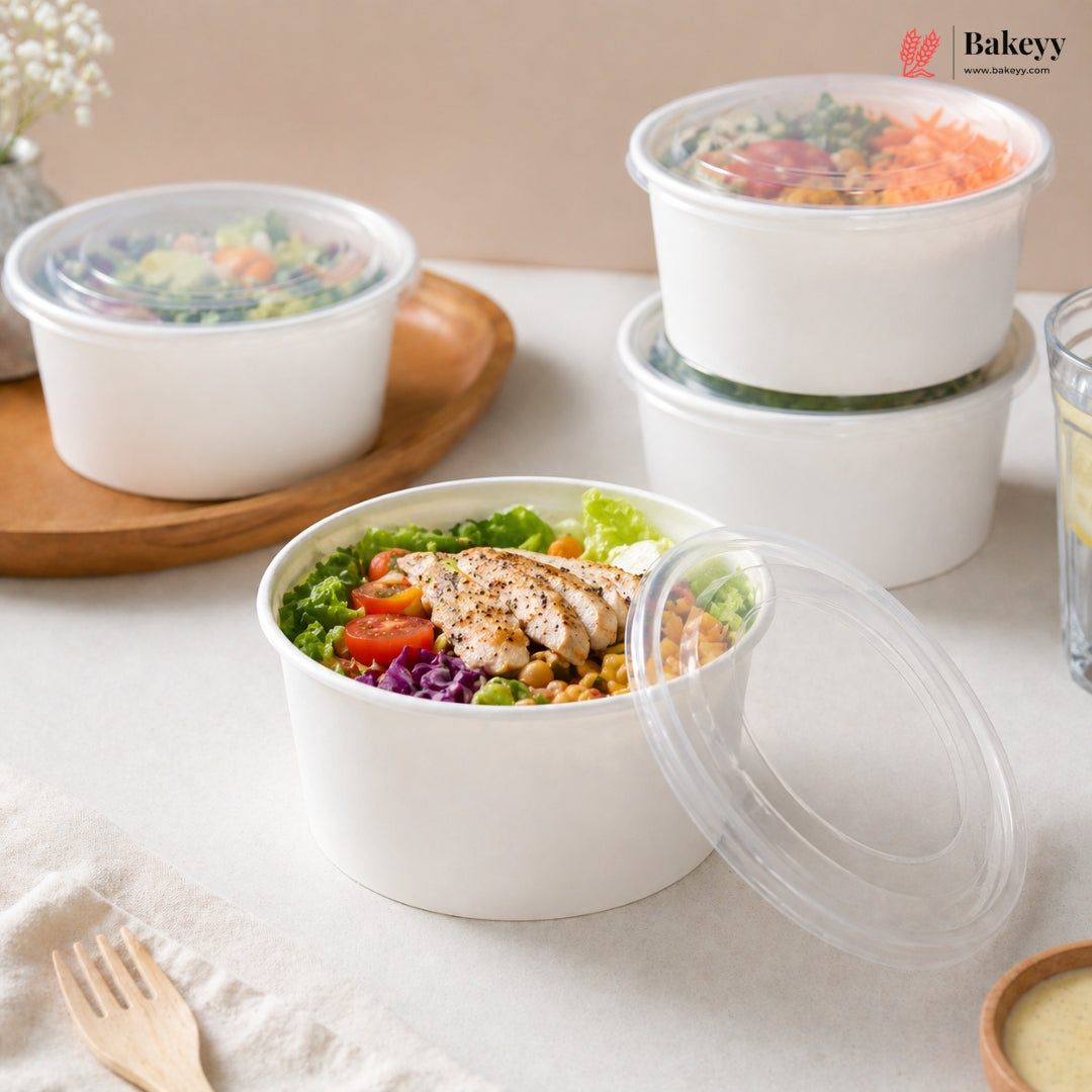White food containers with lids filled with salads on a light surface, featuring the Bakeyy brand.