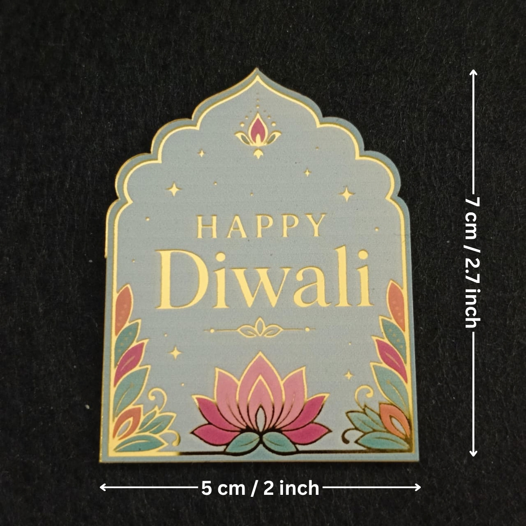 A decorative arched plaque or sign with 'HAPPY Diwali' in gold lettering, a pink lotus at the bottom, and multicolored leaf motifs around the edges, shown on a black background with dimension arrows indicating 5 cm by 7 cm.