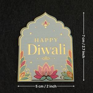A decorative arched plaque or sign with 'HAPPY Diwali' in gold lettering, a pink lotus at the bottom, and multicolored leaf motifs around the edges, shown on a black background with dimension arrows indicating 5 cm by 7 cm.