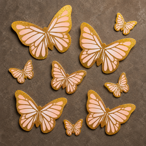 Butterfly-shaped cookies with gold and pink icing on a brown surface