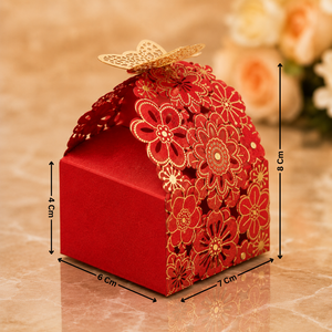 Decorative red gift box with floral designs and gold accents, placed on a reflective surface with a blurred floral background.