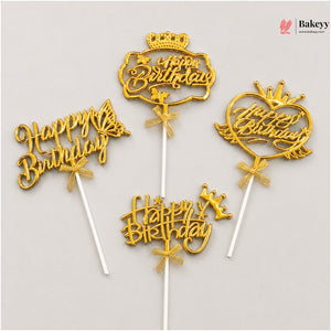 Five gold-colored 'Happy Birthday' cake toppers with different decorative shapes (crown, butterfly, heart, wings) on white plastic sticks, displayed on a light gray background.