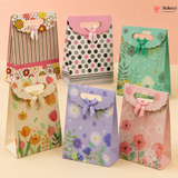Set of colorful paper gift bags with floral designs on a light pink background.