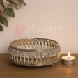 Decorative metal bowl with intricate patterns on a wooden surface next to a lit candle, with 'Bakeyy' branding.