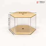 A hexagonal clear acrylic display box with tan cardboard-like base and top panels, shown on a white background with overlaid dimensions: 16 cm / 6 inch across the top, 10 cm / 4 inch height, and 8 cm / 3 inch depth. Bakeyy logo appears in the top right.