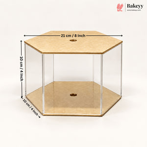 Hexagonal acrylic display case with a light wood top and bottom, shown with dimension lines indicating 21 cm / 8 inch across the top, 10 cm / 4 inch height, and 10 cm / 4 inch depth. The Bakeyy logo is visible in the top right corner.