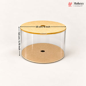 Clear cylindrical cake or pastry display container with a light wood lid and base, shown on a white background with dimension arrows indicating 15 cm / 6 inch diameter and 9.5 cm / 3.