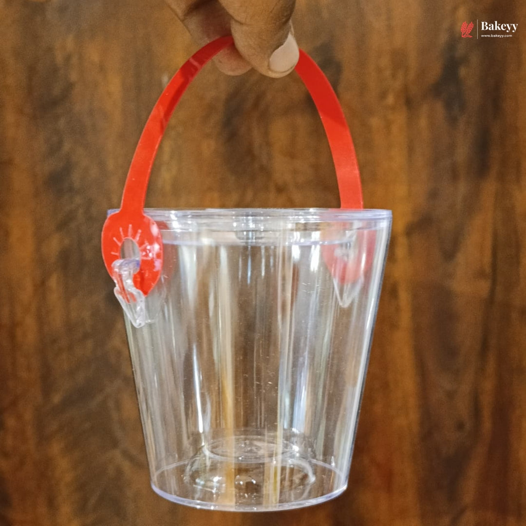 Clear plastic bucket with a red handle held by a hand against a wooden background