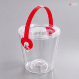 Clear plastic ice bucket with a red handle on a gray background