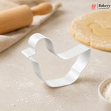 Metallic bell-shaped cookie cutter on a baking surface with a rolling pin and dough in the background, featuring the Bakey brand.